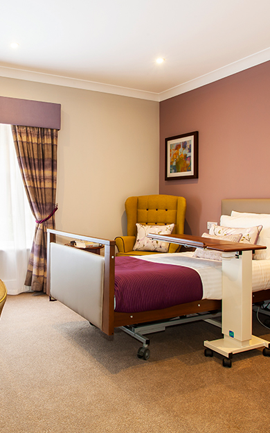 Nursing bed and armchair in a bedroom at Penrose Court Care Home