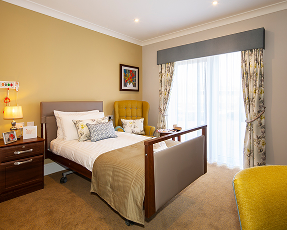 Profiling bed, bedside table and armchair in a bedroom at Penrose Court Care Home