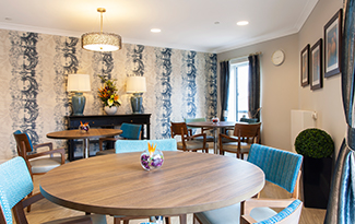 Round wooden tables and blue dining chairs in a dining room at Penrose Court Care Home